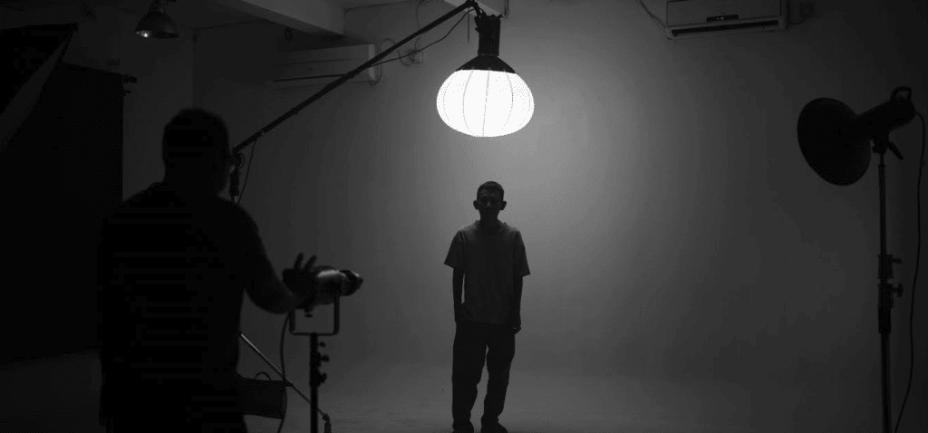 black and white photo of a man standing under a large round light on a stark white film set
