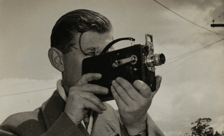 sepia-toned vintage photo of a man holding an old film camera