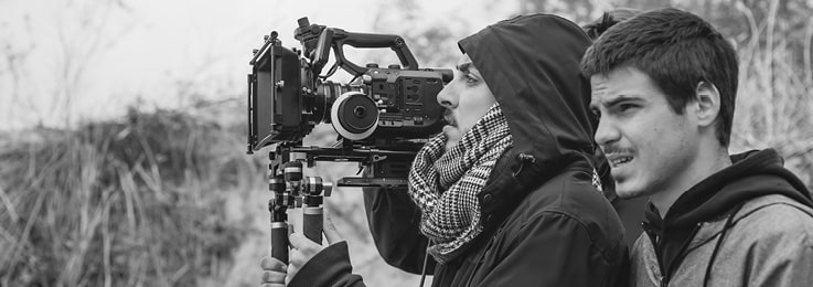 Two men on the beach, one of them holds a large film camera on his shoulder. Maybe he is filming a documentary. Write your documentary script using Celtx (sometimes misspelled as celtix or celtex) screenwriting software