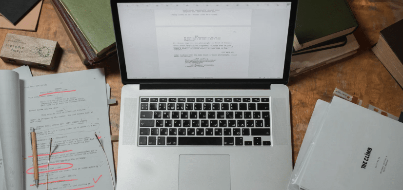 a laptop open to a screen with a screenplay on it. scripts and edited screenplays sit around the laptop.