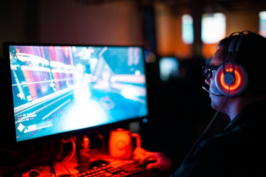 A man wearing headphones playing video games on a computer. What does an executive producer do in video games?