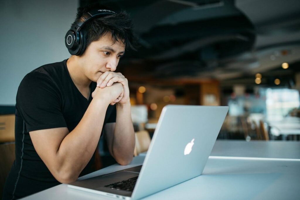 A man wearing headphones, focused on the screen of his open MacBook. Perhaps he is learning how to format a screenplay.