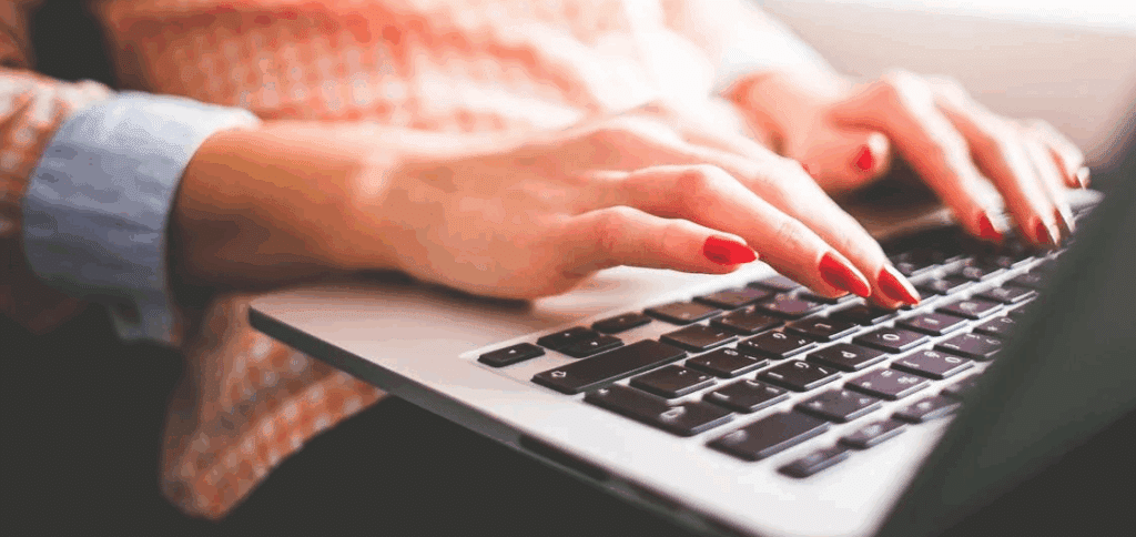 a woman's hands typing on a laptop keyboard.