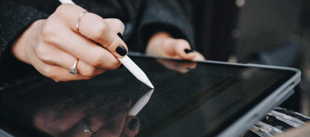 A person with black painted nails uses a stylus on an ipad (or tablet)