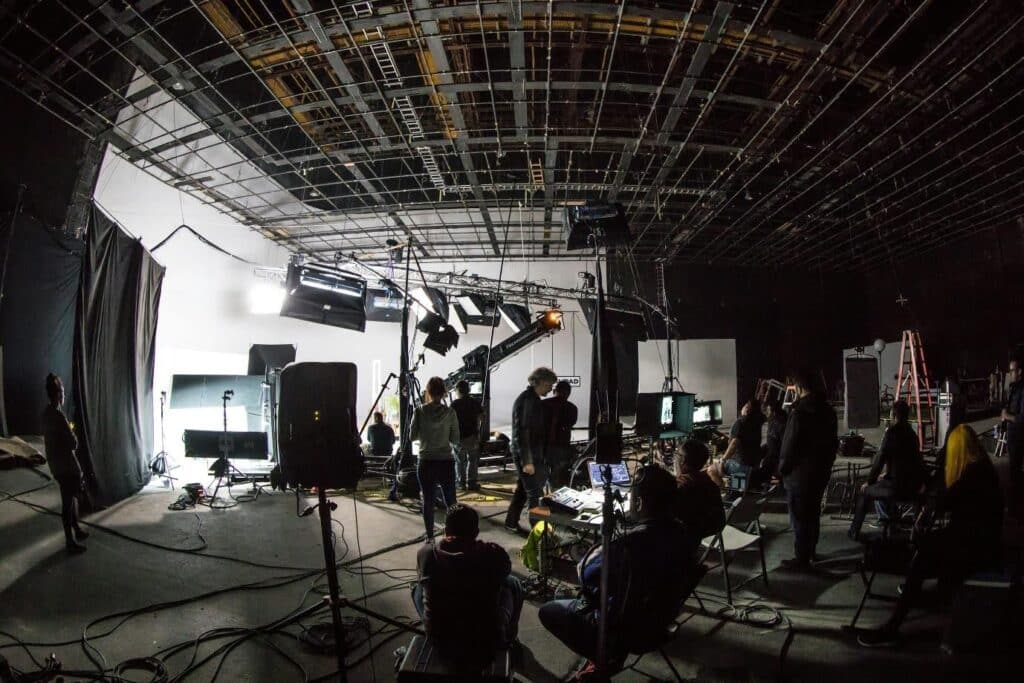 A behind the scenes photo showing a film set. You can see lighting rigs, sound equipment, producers, DPs, and more.
