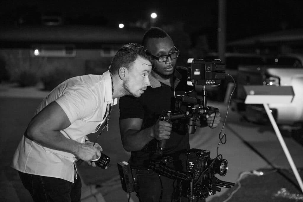 A photo showing two men on a film or television set peering into a camera to set up their shot.