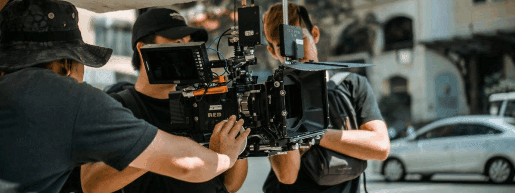 three dudes on an outdoor film set holding a camera.