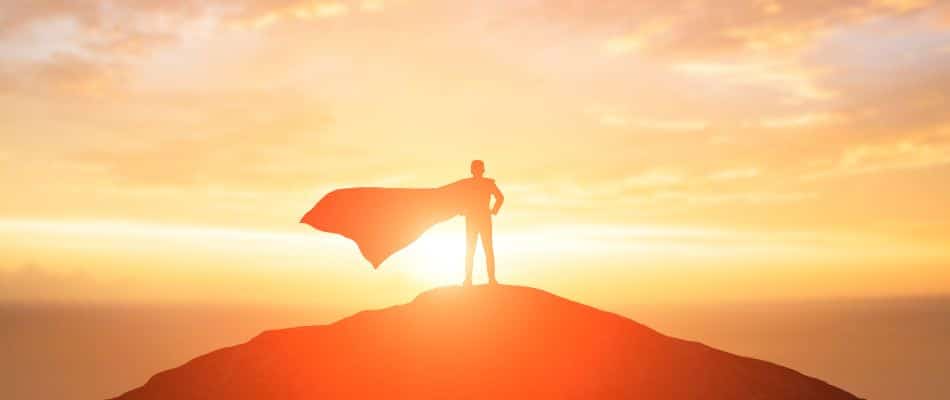 The protagonist of the story stands victorious at the top of a mountain while wearing a cape.