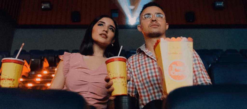 Two people in a movie theater with popcorn and drinks in hand