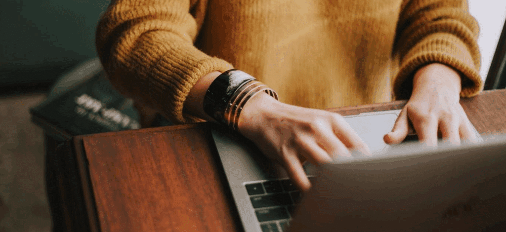 a person typing on a laptop - they're wearing a yellow sweater but their face is not visible.