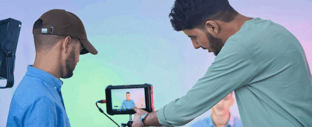 two men on a film set watching playback in the screen of a camera