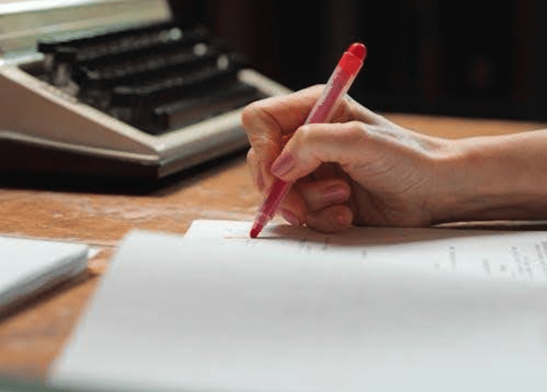 A person editing a screenplay with a red marker.