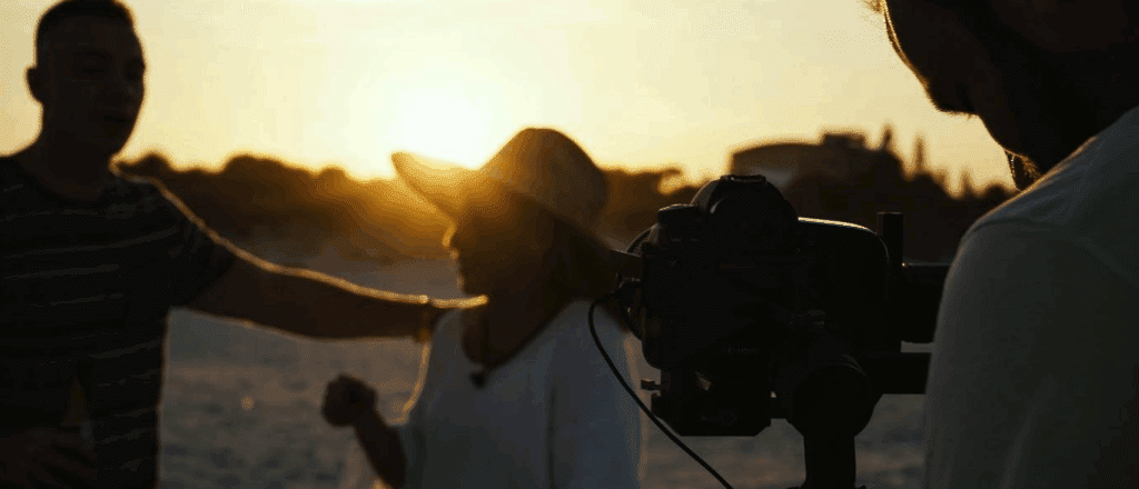 a crew films a documentary. this scene appears to be on a beach.