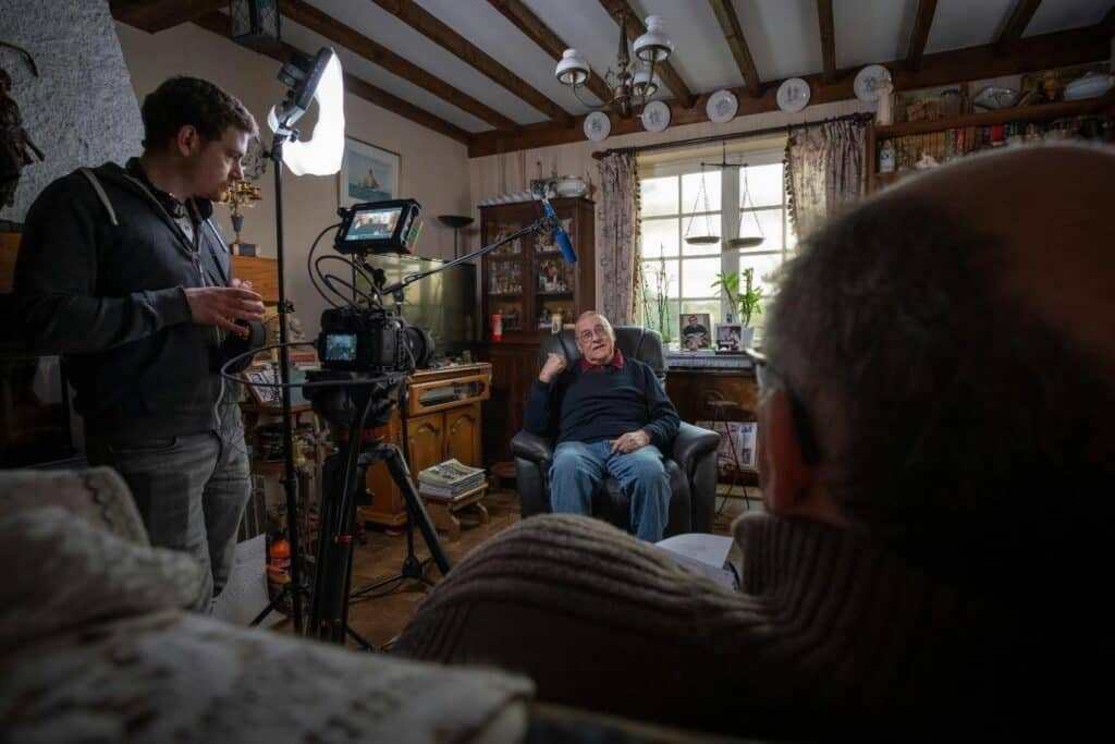 a documentary film crew filming an interview with an older gentleman in his home.