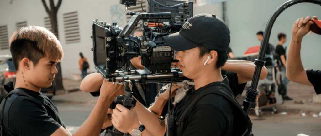 on the set of an indie film. One man holds a camera while a group of others help him adjust it for the scene.