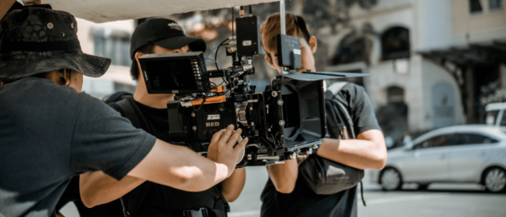 a photo behind the scenes of an indie film. You see a small group of people operating a film camera.