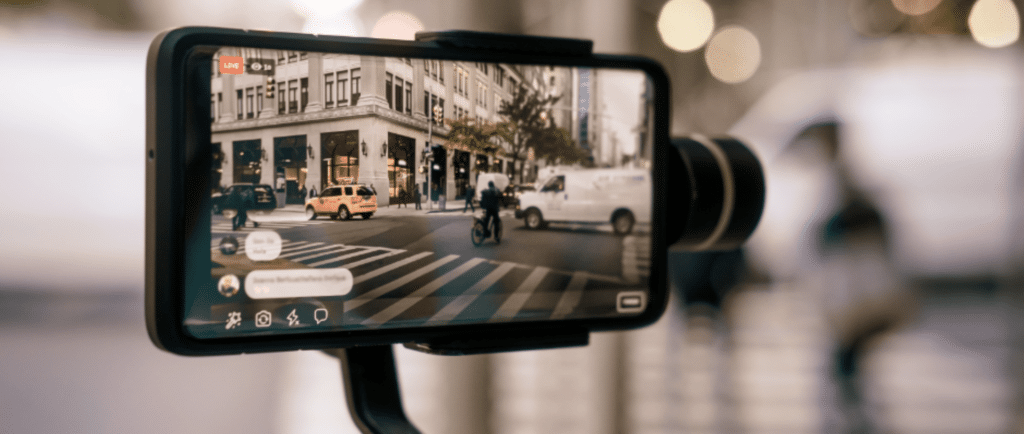 A camera filming an indie film. On the camera's screen is a busy street with a corner shop.