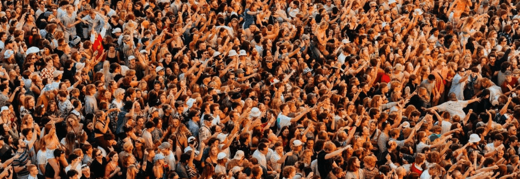 A crowd of people, some with arms up, some holding up phones, some sitting on shoulders. Probably a festival of some sort.