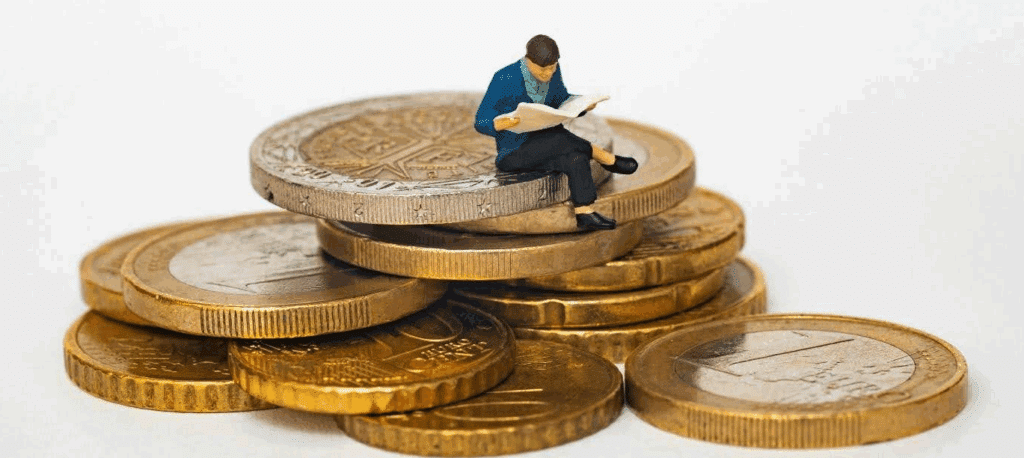 a tiny figurine of a man sits on top a stack of gold coins.