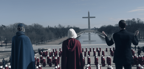 a still of Gilead - a non-personified antagonist - in the final season of The Handmaid's Tale. A large cross can be seen in place of the Washington Monument. Handmaids kneel.