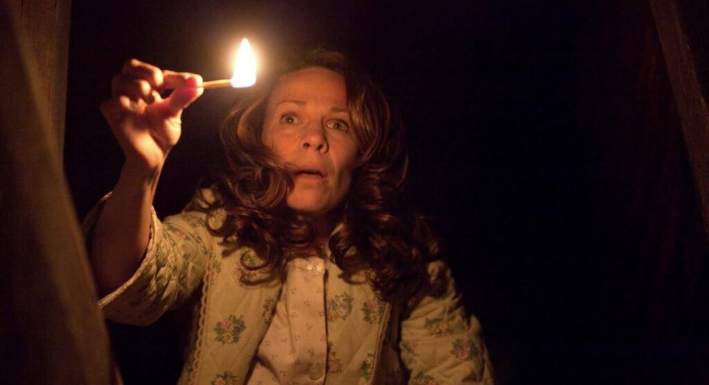 A still from the film The Conjuring: the mother peers down the basement stairs with a lit match.