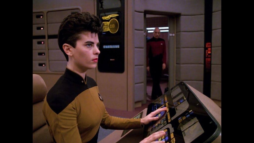 A flat character from Star Trek: The Next Generation (a woman sits in front of a control console with Captain Picard in the background)