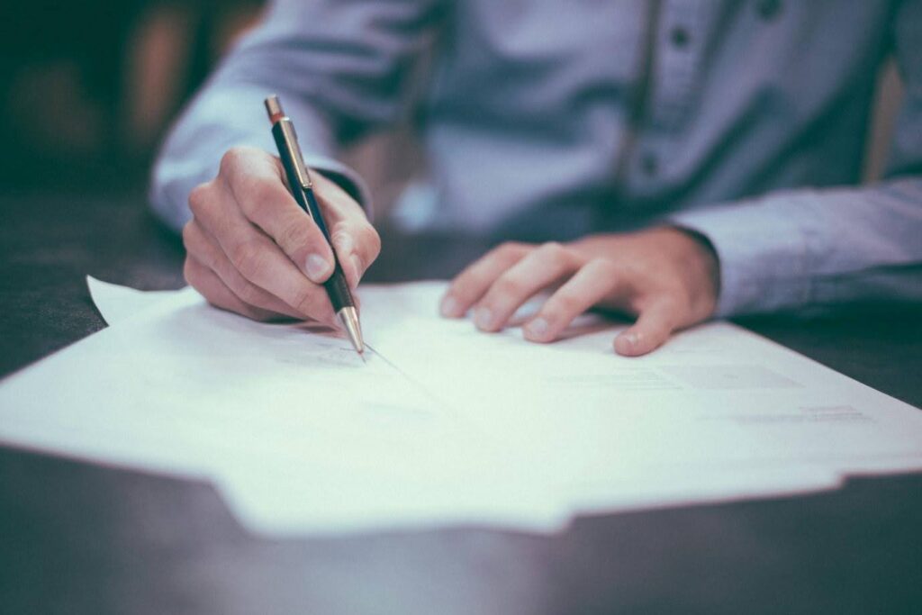 An image that shows a close up of two hands grasping a pen and writing on sheets of paper - this could be you writing the synopsis for your script using Celtx (sometimes misspelled as Celtix or Celtex)