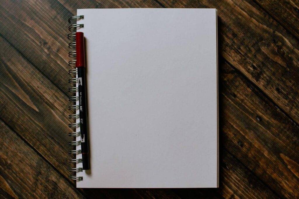 A notebook opened to a blank page with a pen - ready to start writing your screenplay's one sheet. Get started today with Celtx (often misspelled as celtix)