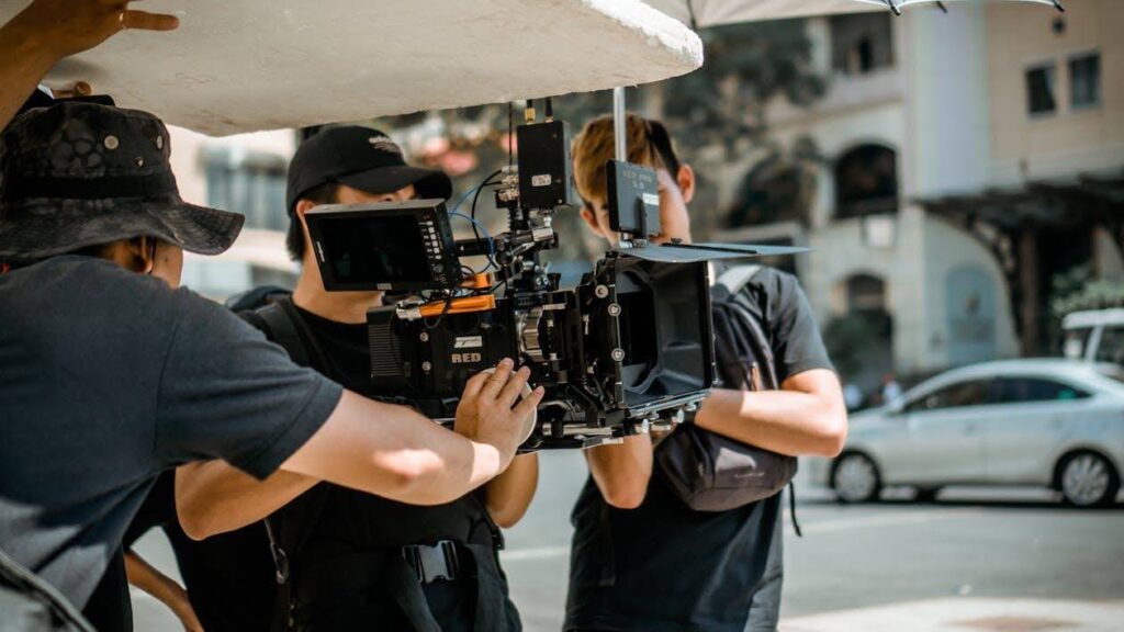 A cinematographer (also known as a D.P.) on set behind the camera with other crew members.