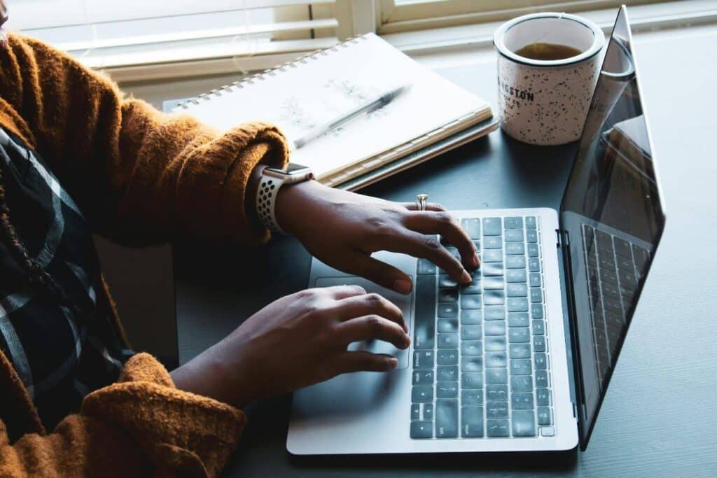 a woman working on a film treatment on a laptop. She has a notebook and a cup of tea beside her.