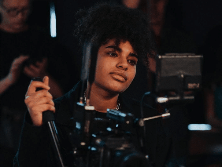 A cinematographer stands behind a film camera.