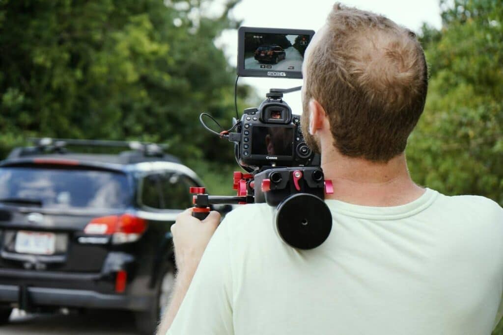 A man holds a camera on his shoulder while filming an SUV driving.