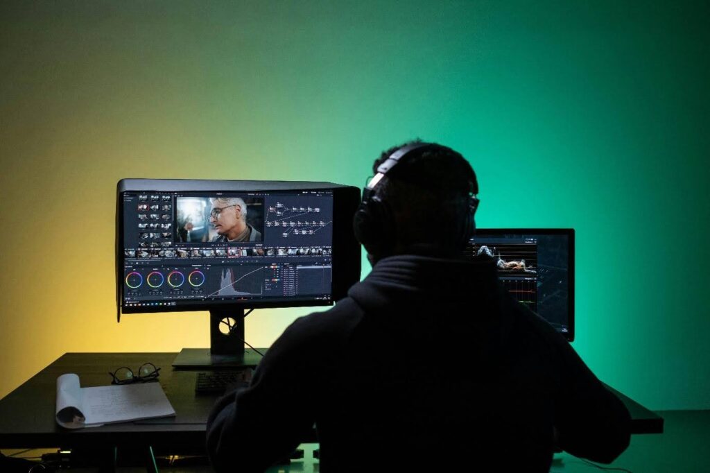A video editor sits in front of a computer with editing software on the screen.