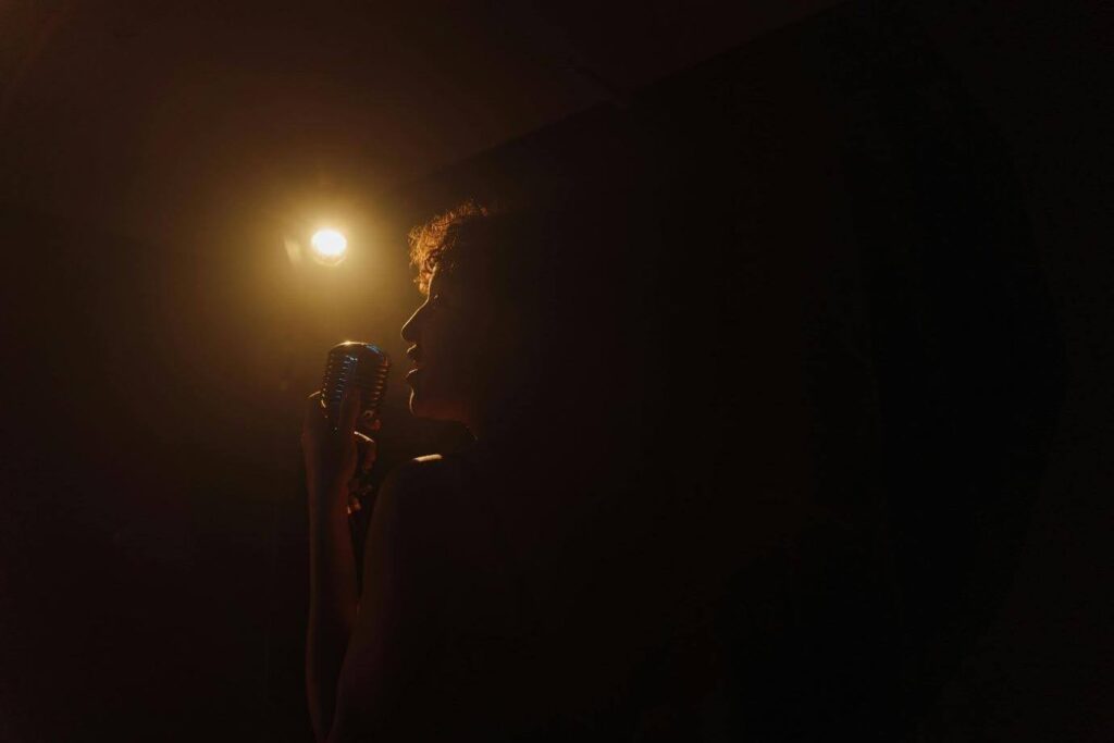 A person sings into a microphone on a dimly lit stage.