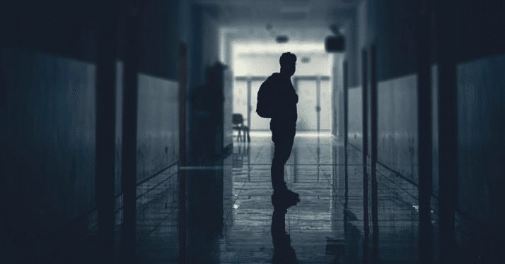 an example of leading lines in film and photography: a person stands in the center of a hallway, the line of lockers and lined floors framing them.