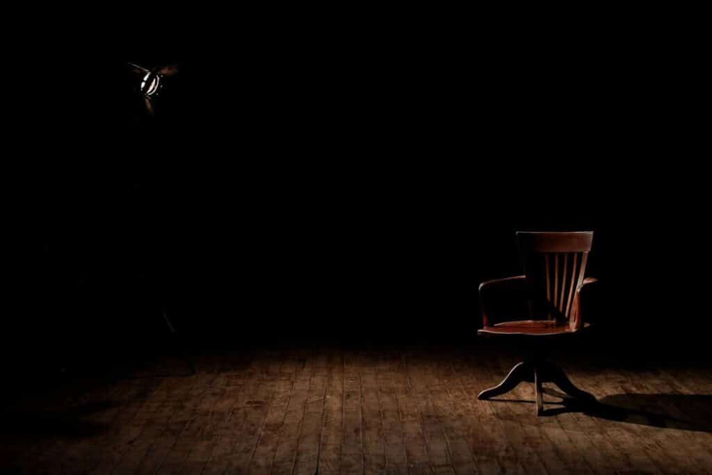 A single empty chair sits on a stage, illuminated by one spotlight.