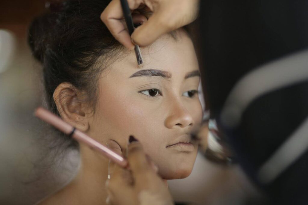 A makeup artist applies concealer around the eyebrow of a young girl