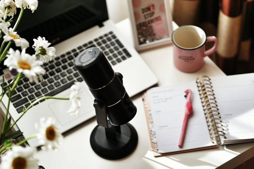 podcast setup: a desk, a microphone, a laptop, a notebook and pen, and a mug of coffee or tea.