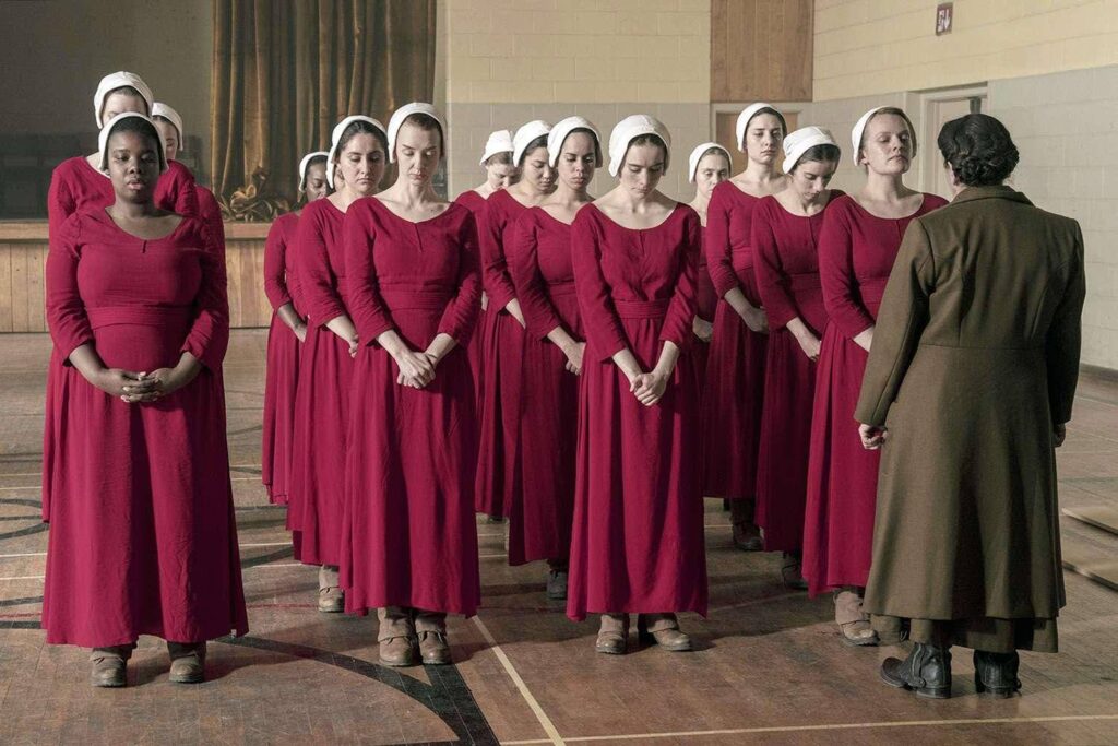 Handmaids dressed in red, being spoken to by Aunt Lydia