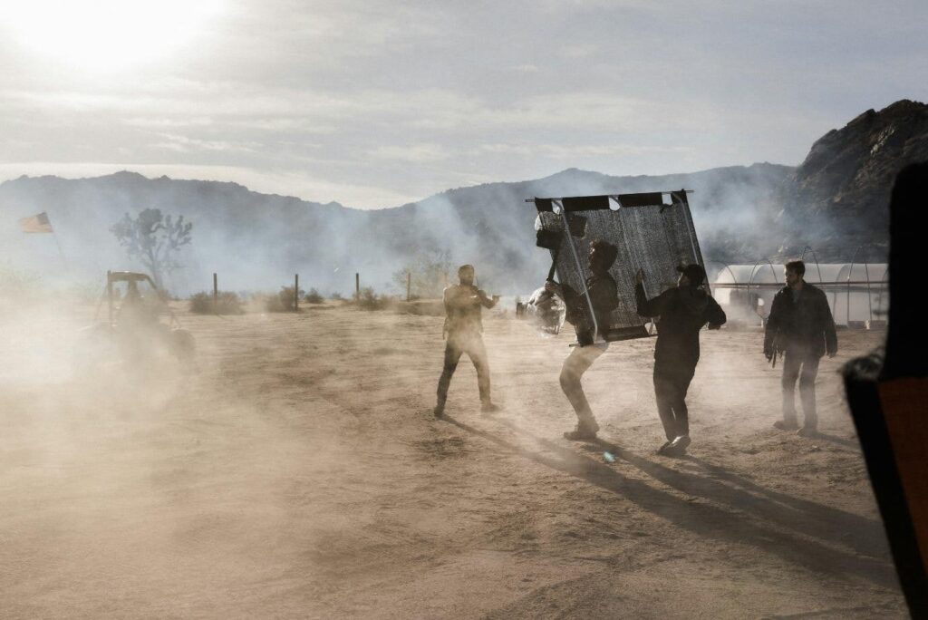 A camera crew films a scene outdoors on a dusty patch of land