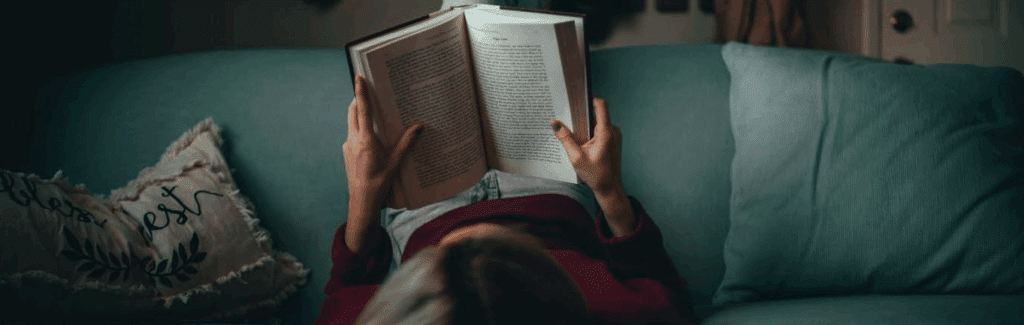 A woman lying on a couch with an open book in her hands.