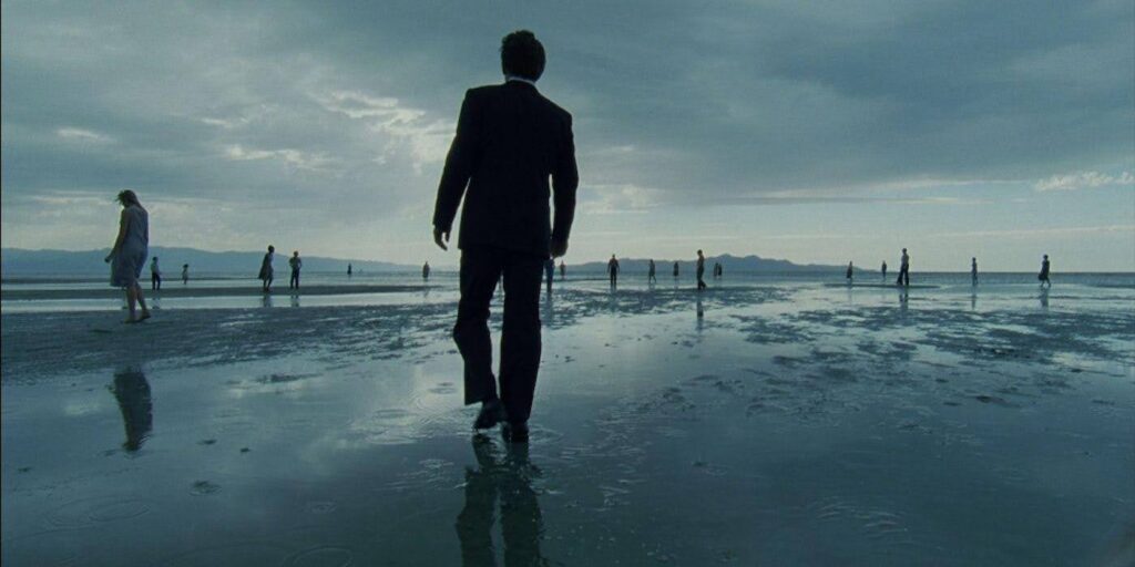 Many people walking aimlessly on a beach or a wet sand flat.