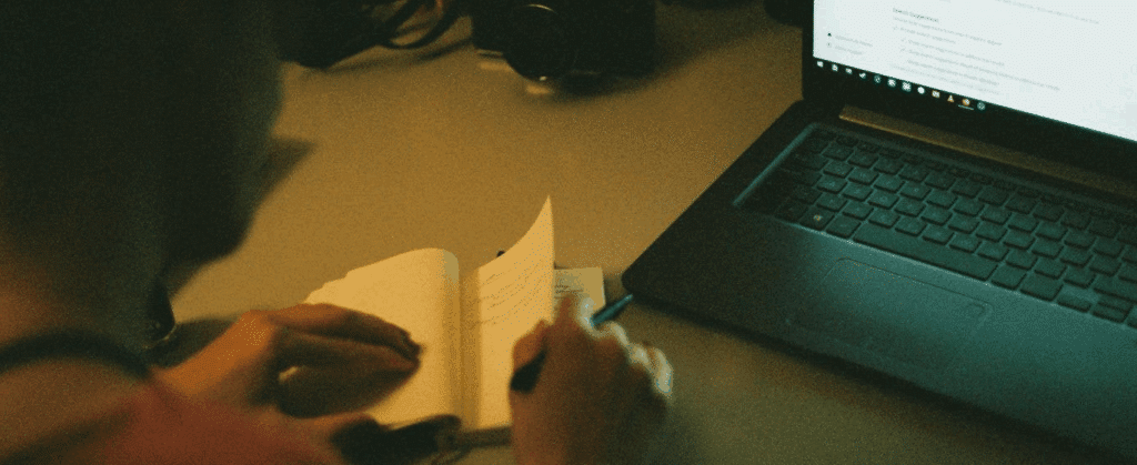 A person sits in front of a laptop, taking notes.