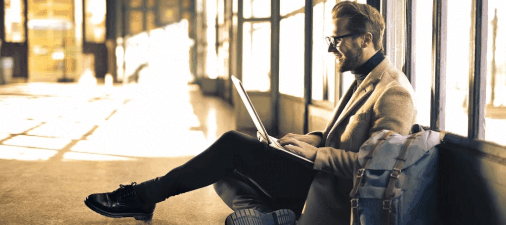 A man sits on the floor with a laptop - looks like he's in the middle of traveling. Cloud storage comes in handy for that.