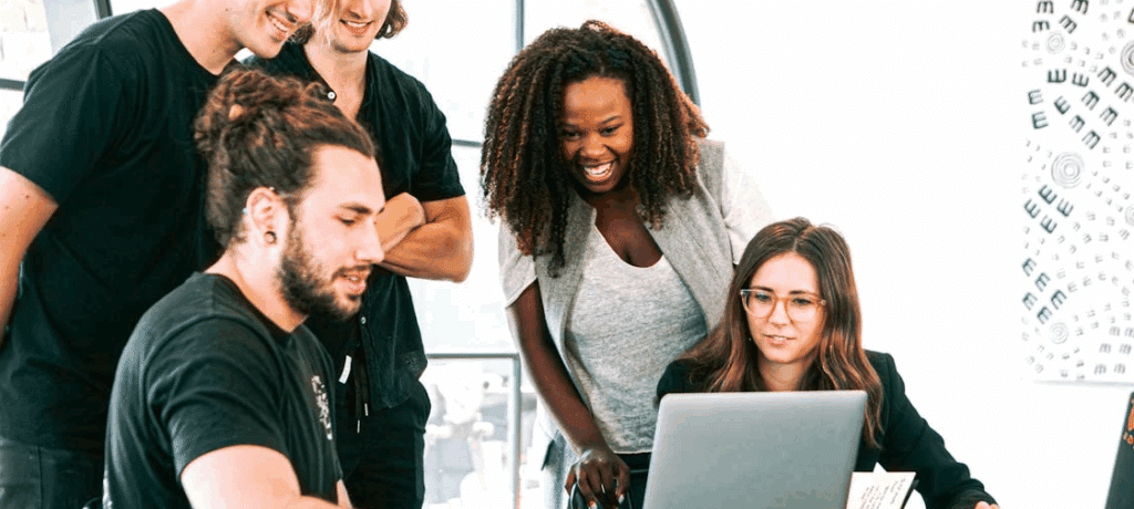 A diverse group of people stand around a laptop.