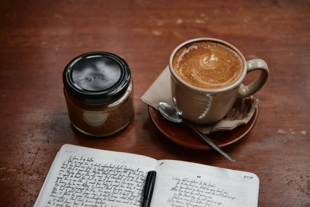 A really hearty cup of coffee sitting by an open journal and what might be a jar of jam?