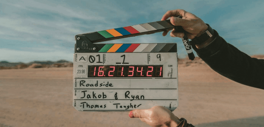 two hands hold up a clapboard in front of the camera in the desert. The clapboard reads that the production is called "roadside" directed by Jakob & Ryan with camera by Thomas Taugher.