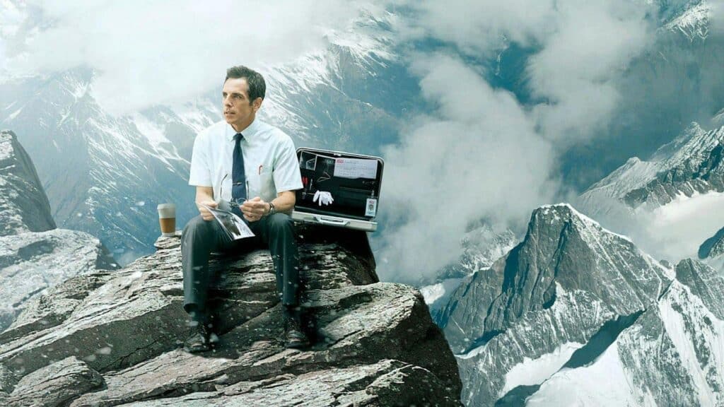 Ben Stiller as Walter Mitty sits atop a mountain with a briefcase and a coffee.