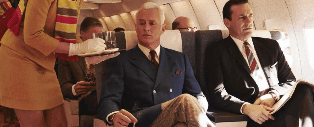 Don Draper on a plane with the handsome man with white hair (who is smoking a cigarette while being served by a flight attendant)