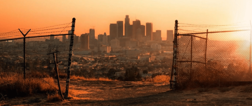 the dusty orange skyline of what appears to be Los Angeles, as seen through a barbed wire fence. How's that for visual exposition?